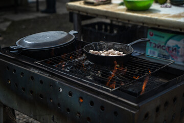 Cooking on a grill, in cast iron cookware, outdoors. Rural food, potatoes with lard.
