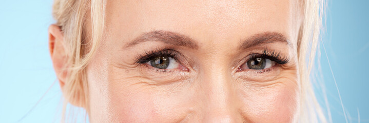 Closeup, eyes and old woman with skincare, cosmetics and wrinkles against blue studio background....