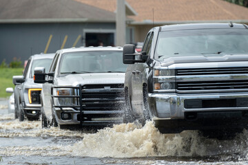 Flooded american street with moving vehicles surrounded with water in Florida residential area....