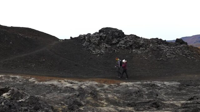 Aerial tracking shot of a couple hiking the black volcanic mountains in Iceland
