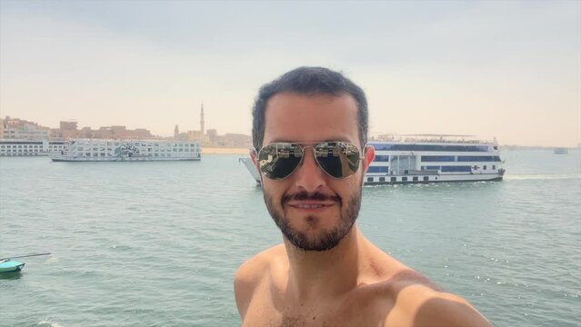TOURIST RECORDING SELFIE NAVIGATING ON THE NILO RIVER, CRUISE SHIPS BACKGROUND