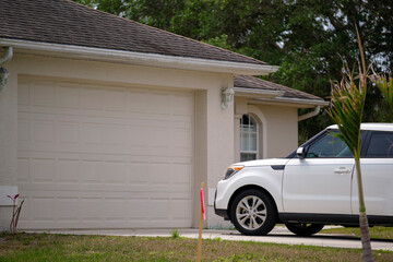 Vehicle parked in front of wide garage double door on paved driveway of typical contemporary...