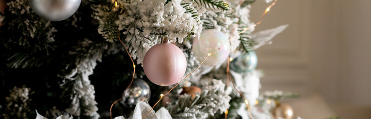 Artificial Christmas tree in a bright interior with silver, pink, bronze balls and snow on the...