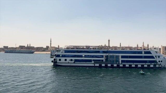 CRUISE SHIP NAVIGATES ON THE NILE RIVER WITH EGYPTIAN CITY IN THE BACKGROUND IN EGYPT