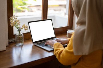 Back view image of a Muslim woman using her laptop in a cafe. A white-screen laptop mockup