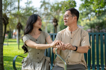 A caring Asian daughter is holding her father's hand to comfort while relaxing in a park together.