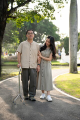 Fototapeta premium A caring young Asian daughter is walking in a green park with her senior dad in the morning.