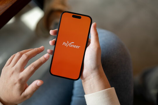 Close-up image of a woman using Payoneer on her IPhone14 while sitting indoors. Financial service