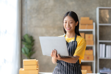 Smiling young Asian business owner woman standing check online orders on laptop computer. Shopping Online concept.