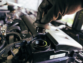 The hand of a car mechanic opens the engine oil cap to inspect before changing the car engine oil ,...