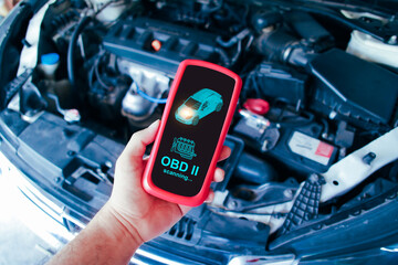 Mechanic man scanning ECU system of car engine by OBD2 wireless scanner tool with a car engine compartment background , Car maintenance service concept