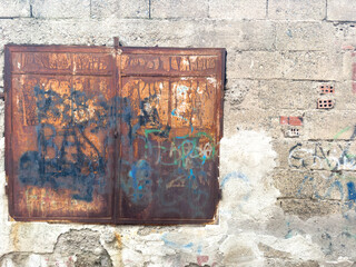 Background with anonymous graffiti on a rusty iron window standing on the wall of a rustic brick house. Thug life, street art in urban. Spray painting masonry background texture.