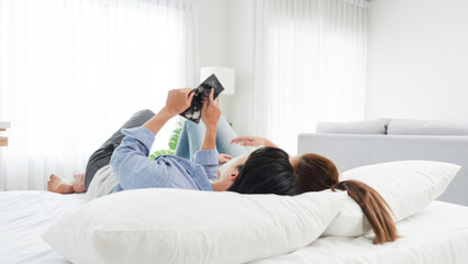 Asian couple family father and pregnant mother see the ultrasound baby image newborn in a next 3 months later while lie down on bed in white bedroom at modern town home