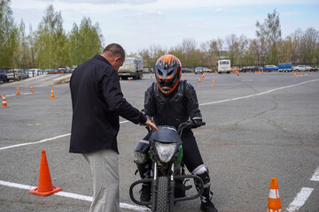 A young woman is learning to ride a motorbike in a motorcycle school. She is taught by a teacher
