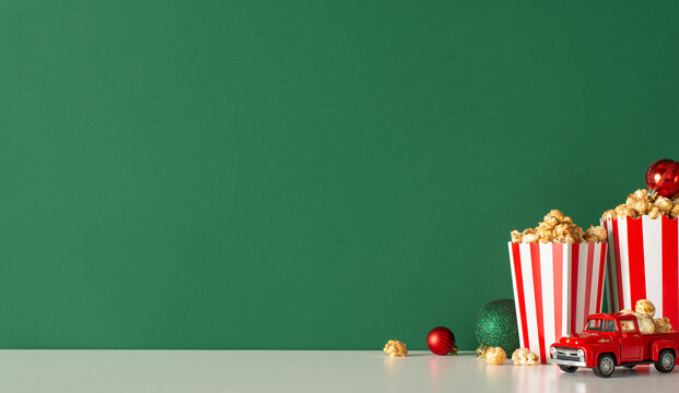 Welcome holiday season with home celebration and popcorn delivery theme. This side-view photo showcases tabletop with red car, popcorn, balls, green wall background. Space available for movie adverts