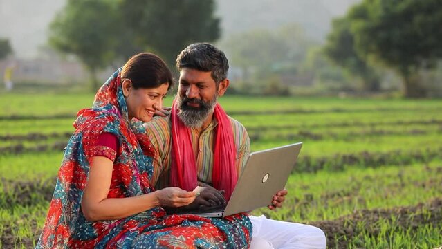 Indian farmer with wife using laptop and bank card at agriculture field.