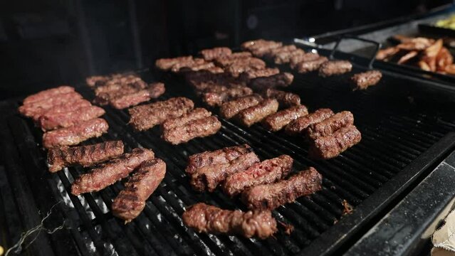 Shallow depth of field (selective focus) details with Romanian traditional mici (mititei), grilled ground meat rolls in cylindrical shape and other meats on the barbecue grill.