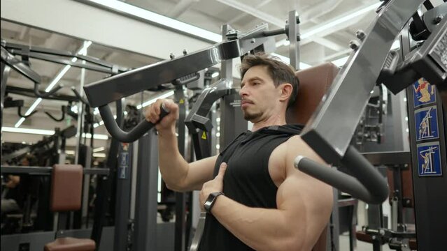 Muscular Man in 40s Doing One Hand Seated Chest Press in Health Club