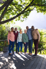 Happy diverse group of senior friends embracing and smiling in sunny garden