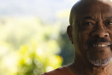 Half face of happy african american senior man smiling in sunny garden, copy space