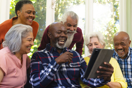 Happy Diverse Group Of Senior Friends Having Video Call And Laughing In Sunny Living Room