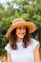 portrait of a young happy brunette in a straw hat. The girl smiles and enjoys her vacation outdoors.