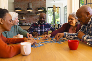 Happy diverse group of senior friends playing with jigsaw puzzles in sunny dining room at home