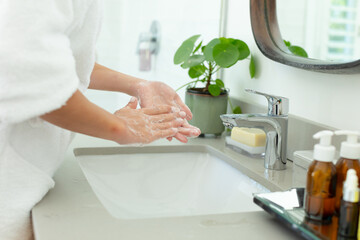 Hands of caucasian woman in bathrobe washing hands in sunny bathroom