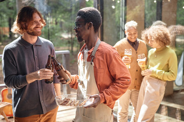 Group of young friends having fun at picnic outdoors, they drinking beer and eating fried meat