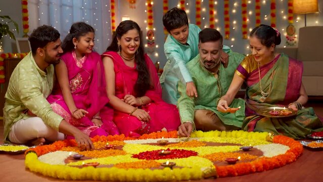 Group of Indian family members decorating Flower rangoli using Diya lamps at home for diwali celebration - concept of holiday gathering, traditional custom and rituals.