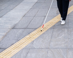 Close-up of the legs of a blind businesswoman walking along a tactile tile with a cane. 