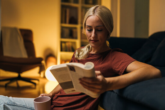 Blond Caucasian woman reading a book in the evening.