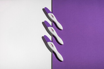 Three positive pregnancy tests on a white - purple background. Close-up, macro, there is space for copying.