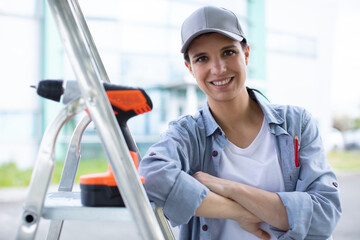 cheerful female sitting with electric drill on stepladder