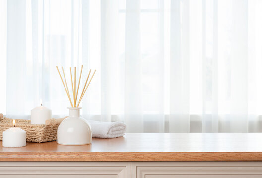 Burning candles, white towel and aroma sticks on table with blurry window curtain background