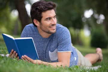 man smilling and lying down in park reading a book