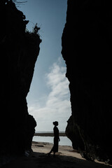 Outline of a girl in a black dress standing between two rocks on the ocean shore
