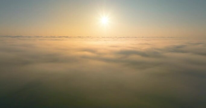 Aerial4K drone in sky is raising above from the thick fog above the beautiful ocean of clouds at sunrise. Sun is rising above the endless sea of clouds until the horizon. Amazing nature landscape