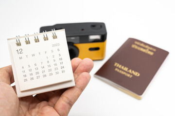 Simple desk calendar for December 2023 on palm. Calendar and holiday concept with passport and camera on the background.