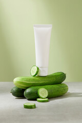 Front view of the unlabeled cleanser tube is placed on top of cucumbers, with a few fresh cucumber...