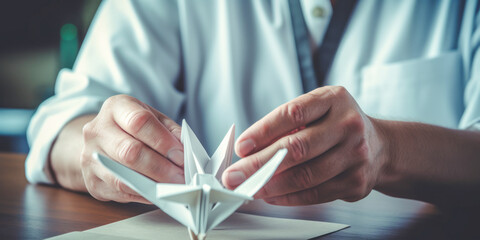 Doctor's hands folding origami crane on desk.