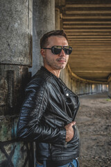 Man in the black leather jacket posing outdoors.