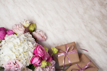 Bouquet of beautiful eustoma, rose and hydrangea flowers with gift on light marble background. Flat lay, top view, space for text.