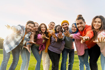 Group portrait of smiling multiracial friends hugging holding hands to camera in park. Happy...