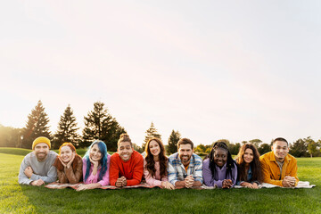 Group portrait smiling multiethnic  friends lying on grass in green park. Happy attractive stylish men and women looking at camera spending time together on nature, copy space.Diversity, friendship 