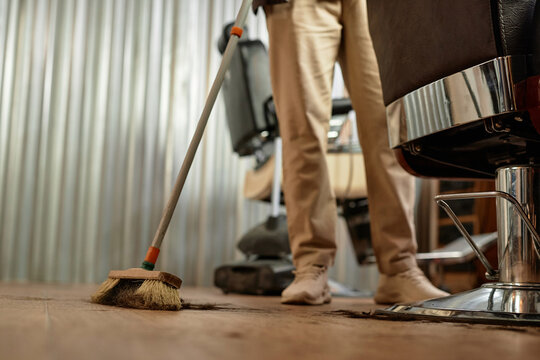 Close-up of barber using broom to sweep after cutting of customer in hair salon
