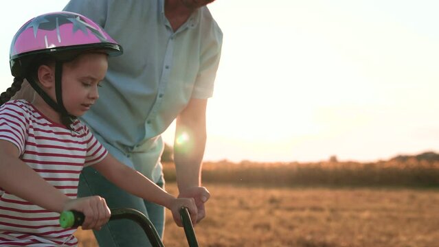 Concentrated little girl rides bicycle caring father holds vehicle in field