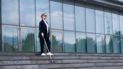 Blind business woman descending stairs with a tactile cane from a business center.