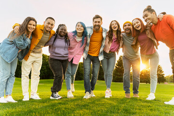 Group portrait of smiling international students hugging wearing looking at camera in university campus. Happy attractive multiracial friends standing together in green park. Diversity, friendship