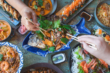 hands with chopsticks eating thai food close up, salads and wok, asian food, top view. Japanese and...